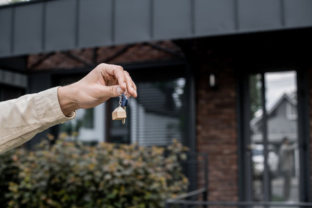 partial view of professional property agent holding key near modern cottage on blurred backgroundの写真素材