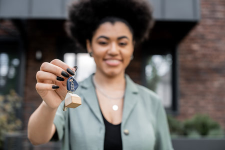 joyful african american property broker holding key from new house on blurred backgroundの写真素材