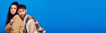 stylish couple in casual wear posing on blue backdrop, bearded man near woman, bold makeup, bannerの写真素材
