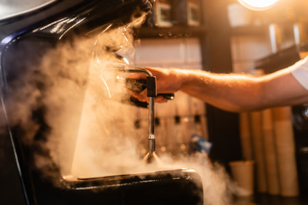 cropped view of barista in apron using coffee machine near steam and lighting in coffee shopの素材 [FY310212196517]