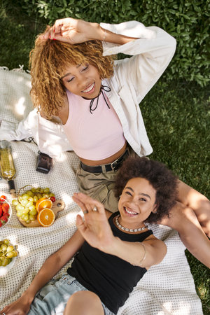 excited african american woman looking at camera near girlfriend with closed eyes, top viewの写真素材