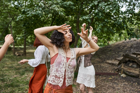 brunette multiracial woman in stylish outfit dancing near on meadow in retreat centerの写真素材