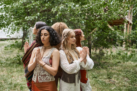 multiethnic women praying while standing back to back outdoors in retreat centerの写真素材