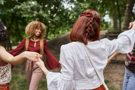 redhead woman in boho clothes holding hands of blurred multiethnic friends in retreat centerの写真素材
