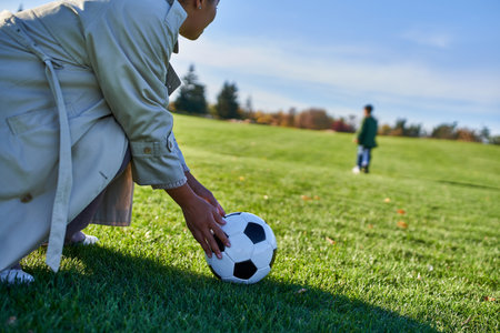 african american woman with soccer ball, mother looking at son, blurred background, green fieldの写真素材