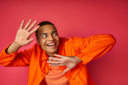 excited and funny african american man gesturing and looking away on red, orange shirt, trendyの写真素材