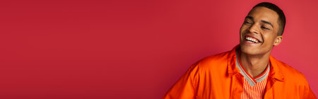 excited african american guy laughing on red background, orange shirt, portrait, banner, copy spaceの写真素材