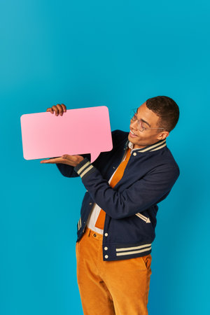 cheerful african american student in trendy casual attire with empty speech bubble on blue