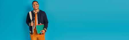 stylish african american student in jacket, with notebooks and backpack on blue, banner, copy spaceの写真素材