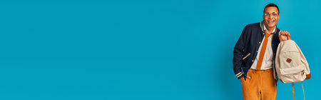 cheerful and fashionable african american student holding backpack on blue, banner, copy spaceの写真素材