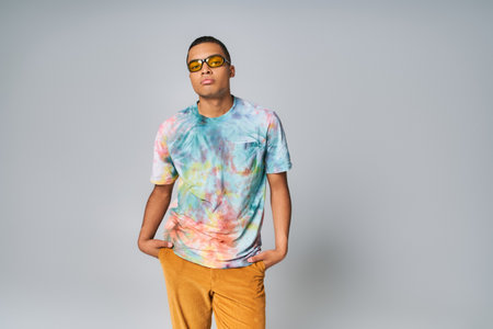 young african american man in sunglasses, tie-dye t-shirt, orange pants on greyの写真素材