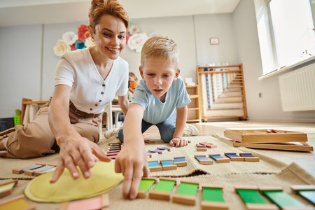 montessori school, blonde boy playing educational game near happy teacher, motion, color matchingの写真素材