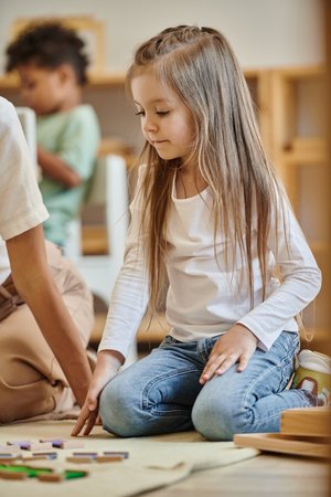 Montessori school, cute girl sitting near educational game next to teacher, preschooler, smartの写真素材