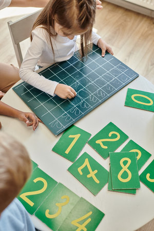 top view of girl writing numbers on chalkboard, learning how to count in Montessori school