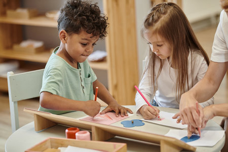multiethnic kids drawing with pencils near teacher during lesson in montessori schoolの写真素材