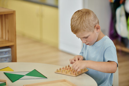 boy playing with rubber bands and wooden board on table during lesson in montessori schoolの写真素材