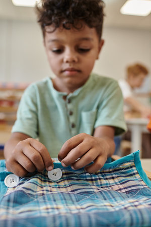 blurred african american boy playing with cloth and buttons on frame in montessori schoolの写真素材