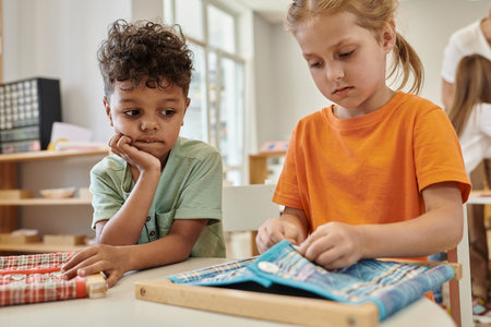 african american boy looking at friend playing with cloth and buttons in montessori schoolの写真素材
