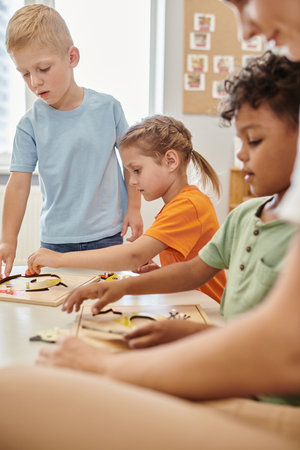 multiethnic kids and teacher using didactic materials during lesson in montessori school