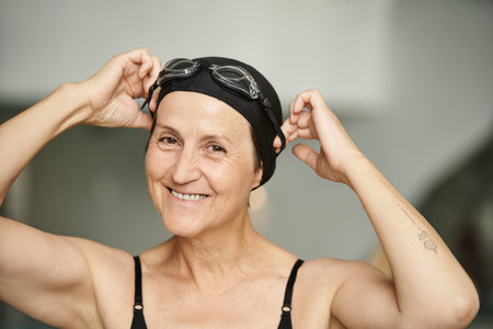 portrait, active lifestyle, mature woman in swimwear, adjusting goggles, swim cap, spa, tattooの写真素材