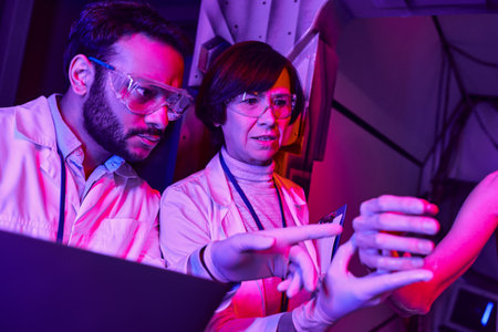 indian scientist with laptop pointing at humanoid alien near middle aged colleague in innovative labの写真素材