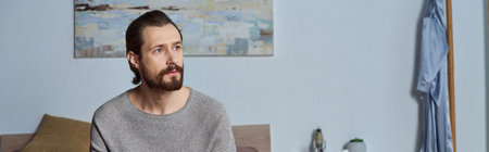 pensive man looking away while thinking about something in modern bedroom, painting  on wall, banner