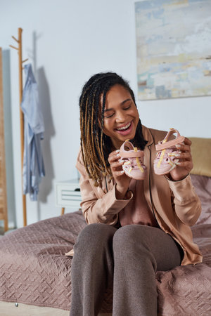 happy african american woman and bearded man holding baby shoes, future parents, expectation, cute