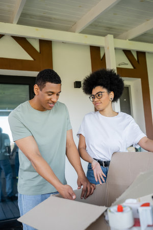 african american woman pointing at carton box near boyfriend during moving in new house