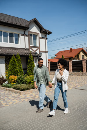 positive romantic african american couple walking on sidewalk on urban street in summerの写真素材