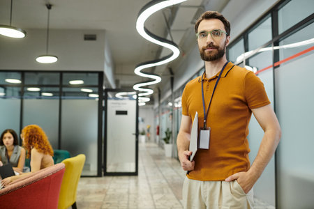 bearded team lead with documents looking at camera near blurred businesswomen talking in office