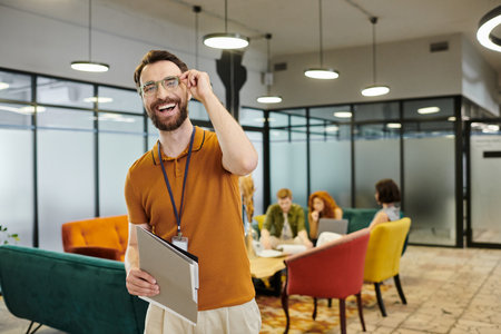 successful bearded entrepreneur in eyeglasses smiling at camera near team talking in modern office
