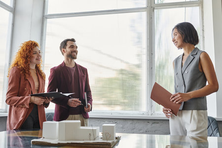business partners smiling near young architect and building model during presentation in office