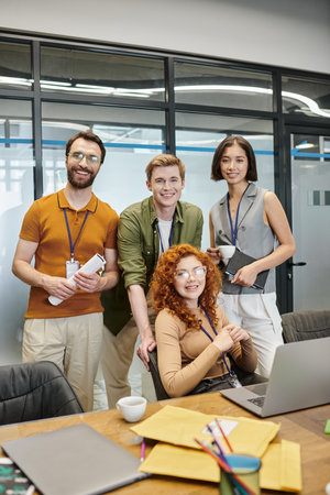 creative team looking at camera near laptop in office, professional headshot, business success