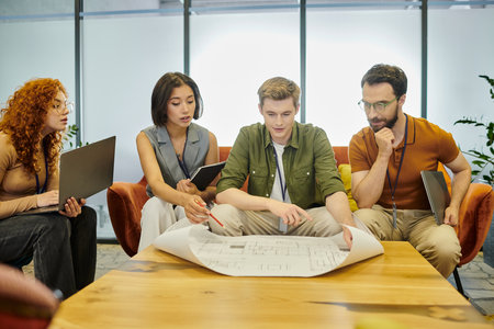 young architect pointing at blueprint near creative business team working on startup in office