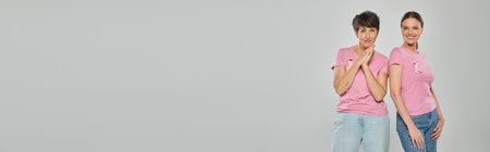 smiling women in pink t-shirts and ribbons posing isolated on pink, banner, breast cancer conceptの写真素材