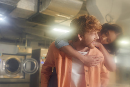 blurred young asian woman piggybacking on cheerful boyfriend in public laundryの写真素材