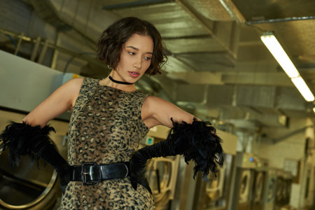 fashionable young asian woman in dress with animal print and gloves posing in coin laundry