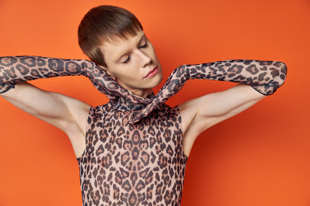 queer model in animal print outfit posing on orange backdrop, closed eyes, stylish genderfluidの写真素材