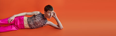 queer person in leopard print top and pink pants lying on orange backdrop, style and fashion, bannerの写真素材