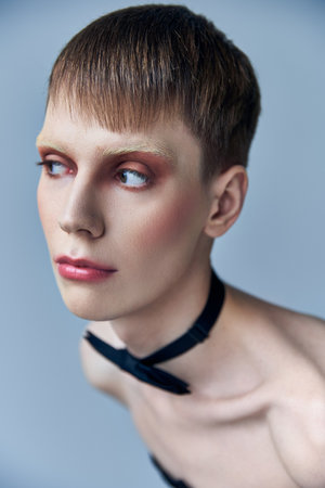 queer model with makeup looking away, grey background, fashion, bow tie, androgynous, portraitの写真素材