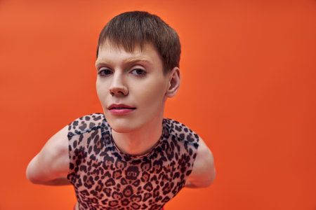 queer model in leopard print sleeveless top looking at camera, orange background, fashion trend