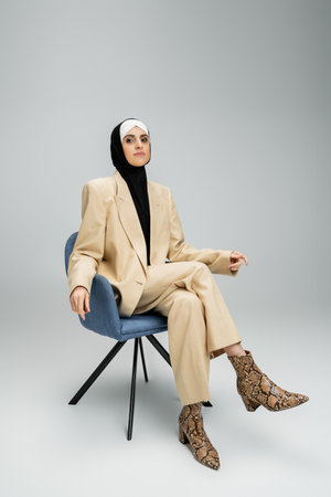 ambitious muslim businesswoman in hijab and beige suit sitting in armchair on grey, bannerの写真素材