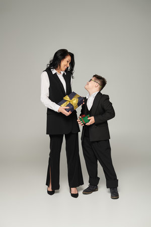 businesswoman and happy son with down syndrome in school uniform holding gift boxes on greyの写真素材