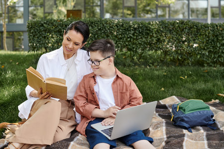 happy middle aged woman reading book near son with down syndrome using laptop in park