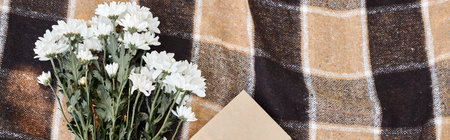 top view of white chrysanthemums and book on plaid picnic blanket, leisure concept, banner
