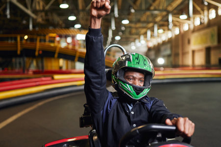 Go kart speed drive indoor race, excited african american driver in helmet celebrating victoryの写真素材