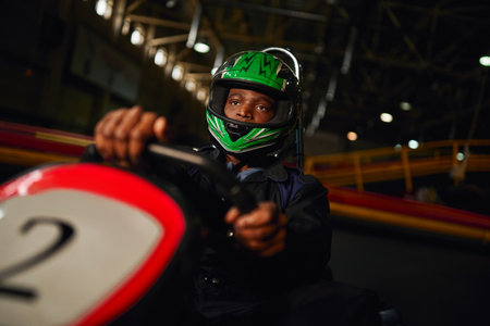 african american go cart racer in helmet driving on indoor circuit, speed racing challengeの写真素材
