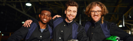 multicultural and joyful go kart racers in protective suits hugging and holding helmets, bannerの写真素材