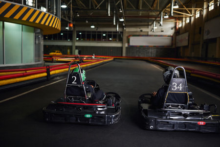 two karting drivers in helmets and sportswear driving go kart on indoor circuit, competitorsの写真素材