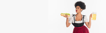 pleased african american bavarian waitress with mug and hot dog on white, bannerの写真素材